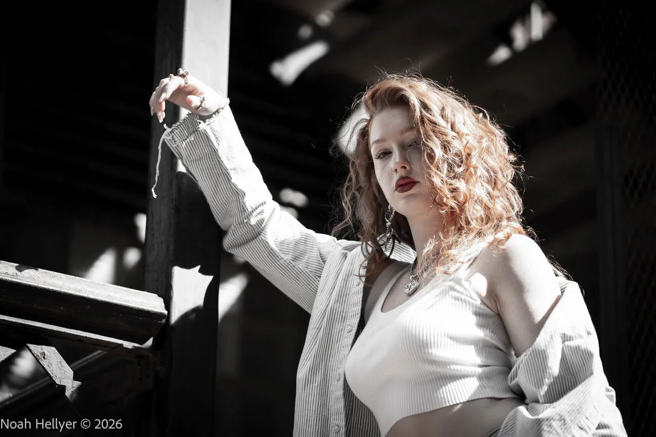 A woman with curly red hair in a white jacket, half in hard sunlight and half in shadow.